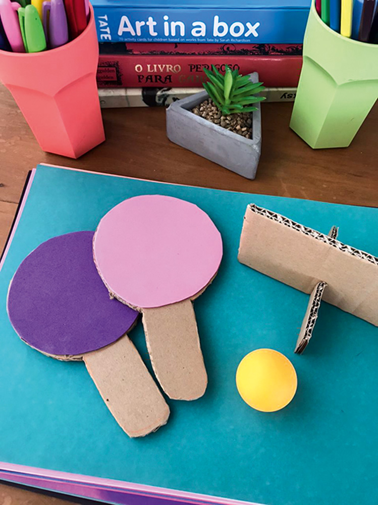 Duas raquetes e uma mesa de pingue-pongue pequena feitas de materiais de papelaria.