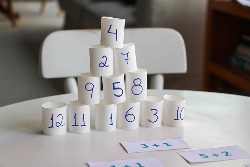 Pirâmide feita com tiras de papel com números escritos. Na mesa, as operações correspondentes a cada linha da pirâmide.
