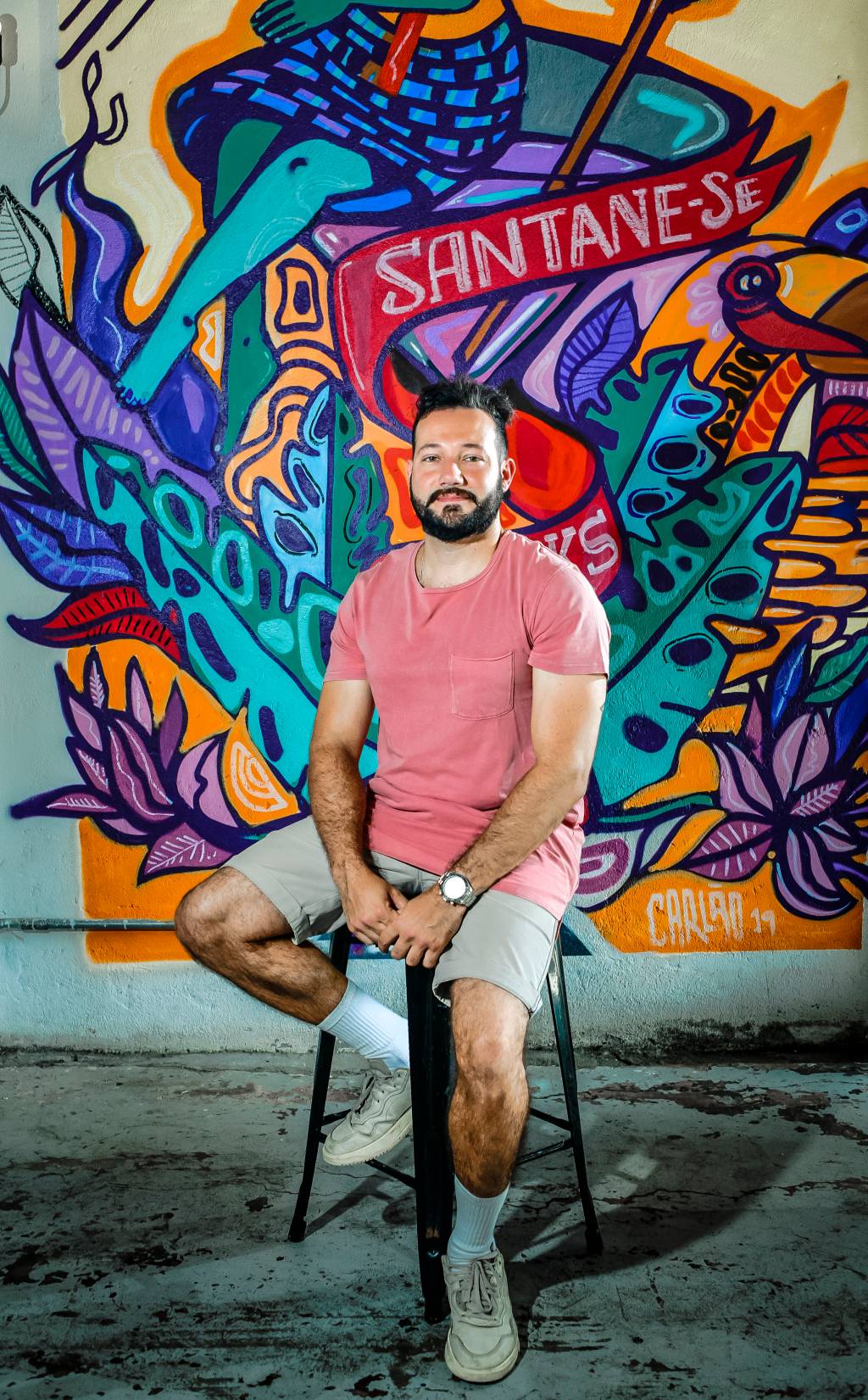 Imagem mostra dono do Degrau Bar, Pedro Fargetti, sentando em banqueta com grafite colorido ao fundo