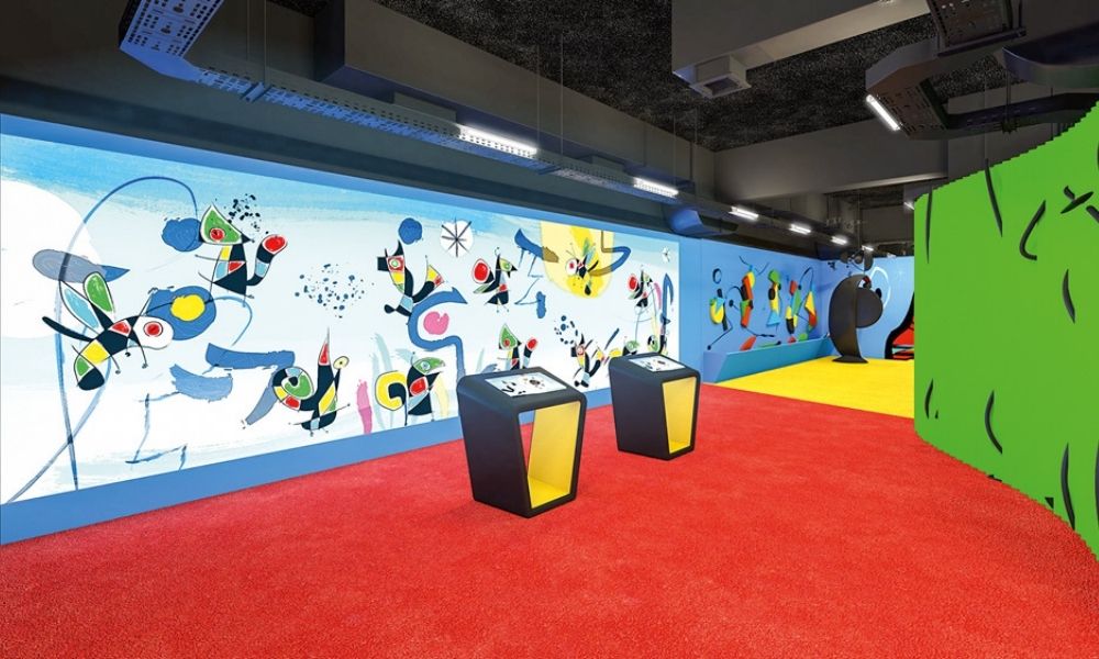 Imagem apresenta parte da exposição "O Jardim das Maravilhas de Miró" em sala com desenhos coloridos e abstratos