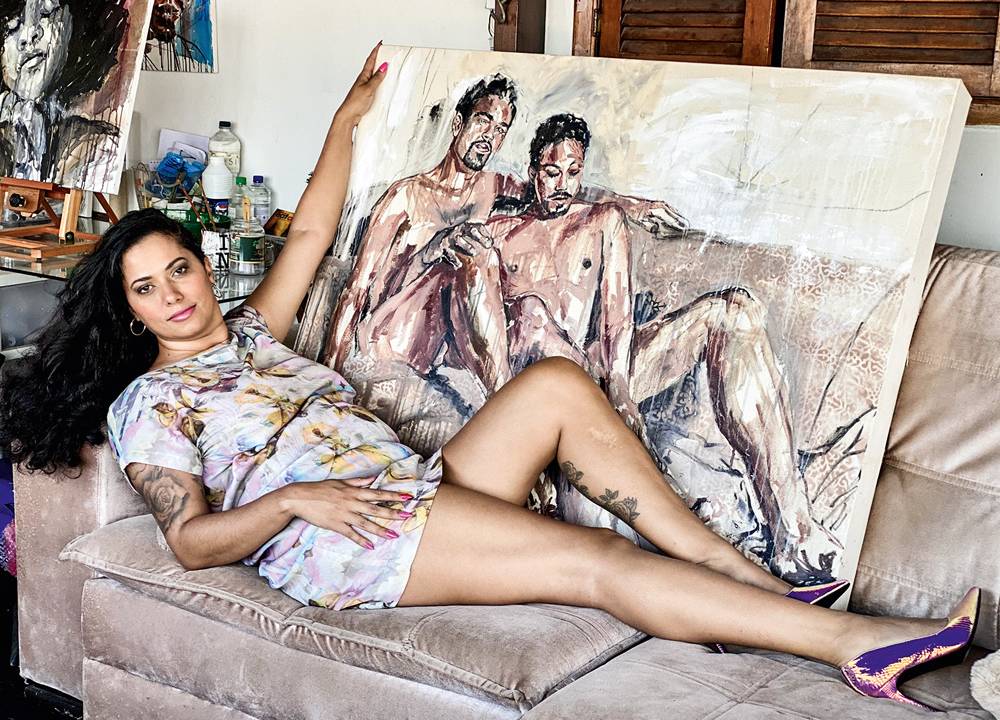 Imagem mostra a artista Panmela Castro segurando uma pintura de dois homens