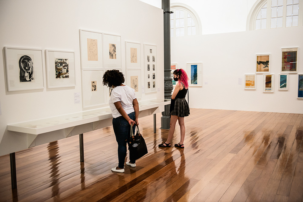 Mulheres olham obras em exposição