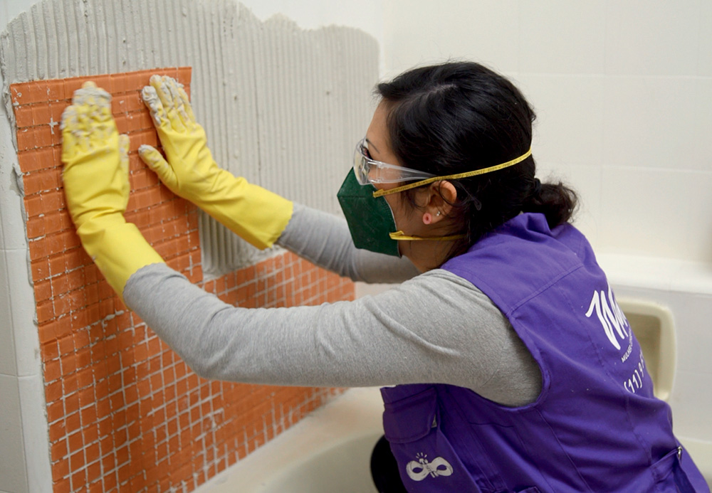Funcionária do Mana Manutenção, empresa de serviços domésticos para mulheres, coloca revestimento em uma parede