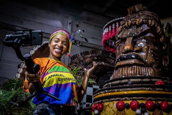 menina em barracão de escola de samba segura celular com pau de selfie