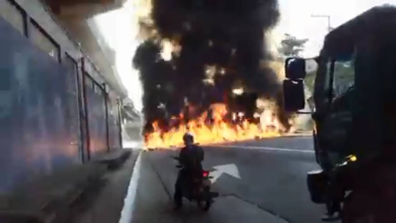 Avenida com pneus queimando em frente aos carros parados