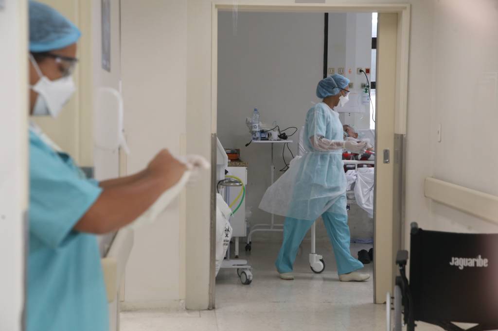 Foto de uma sala de hospital com duas enfermeiras equipadas com roupas contra covid lendo prontuários