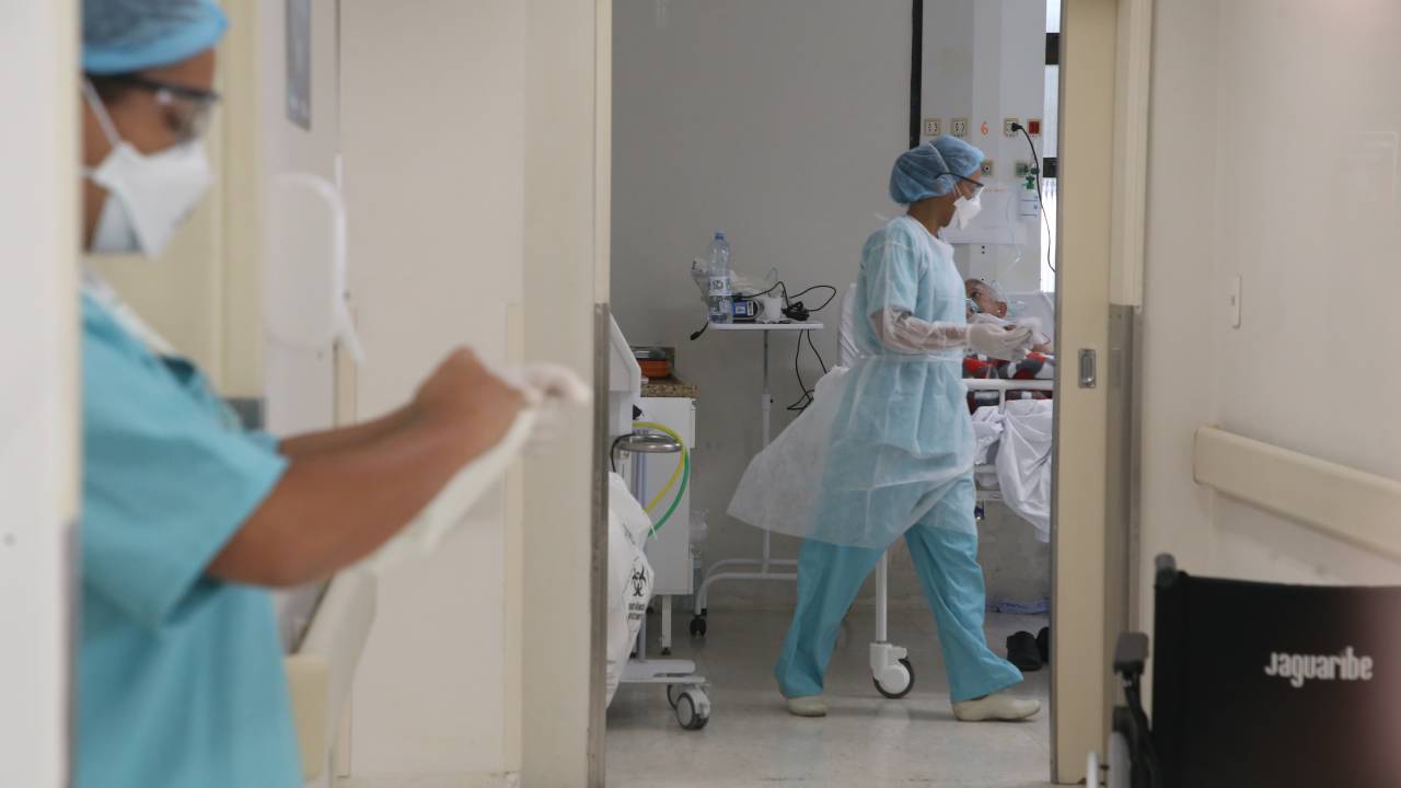 Foto de uma sala de hospital com duas enfermeiras equipadas com roupas contra covid lendo prontuários
