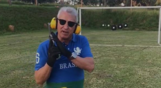 Ricardo Nunes vestindo uma camisa social branca, com um fundo preto, enquanto fala com o público utilizando um microfone e aponta com o braço esquerdo na direção do público.