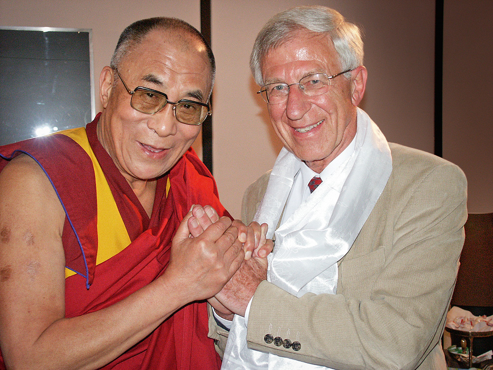 Tenzin Gyatso, o 14º Dalai Lama, com o ativista alemão Franz Alt. Eles posam para a foto de mãos dadas em frente ao peito