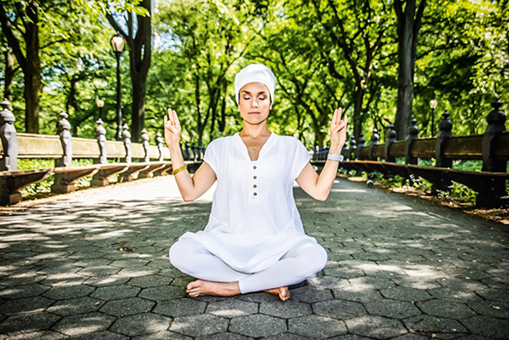 Daniela em pose de meditação, vestida inteira de branco, em um ambiente arborizado e de olhos fechados