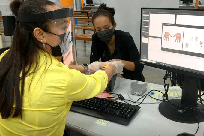 A imagem mostra atendimento em unidade do Poupatempo: mulher estende as mãos para impressão digital