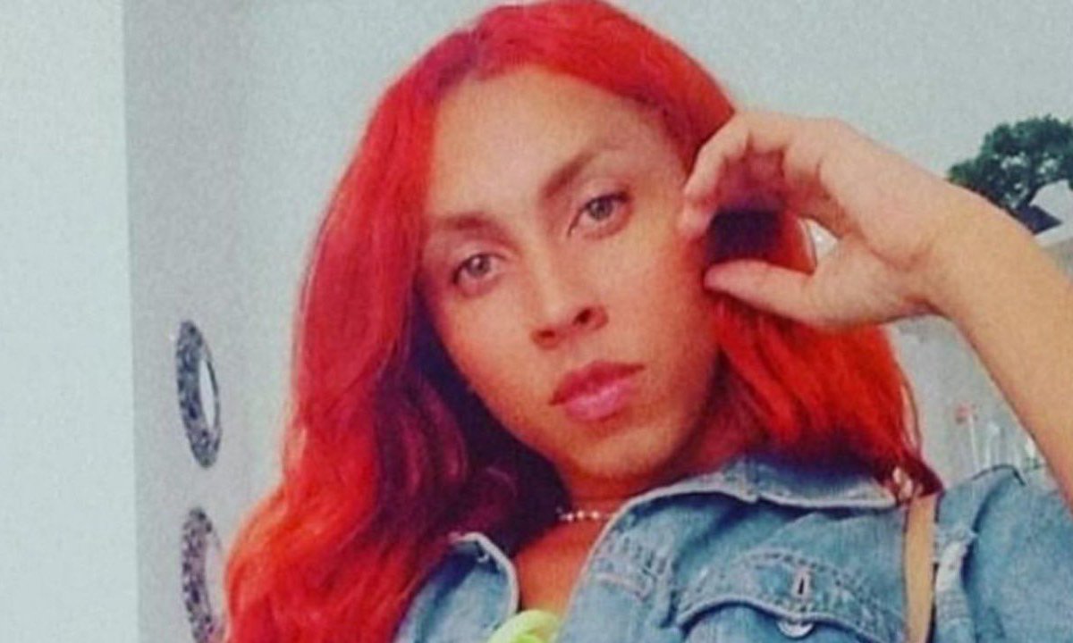 Lorena Muniz, mulher trans morta em clínica, aparece na foto com cabelos vermelhos e jaqueta jeans.