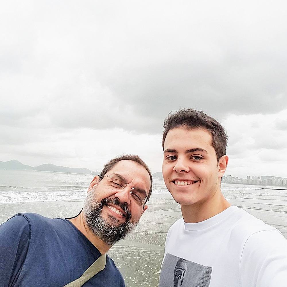 Lucas tira uma selfie com o pai, e na fotografia estão os dois sorrindo com uma praia ao fundo