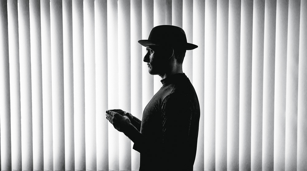 Homem de perfil com as mãos em frente ao peito. Foto escura e preta e branca