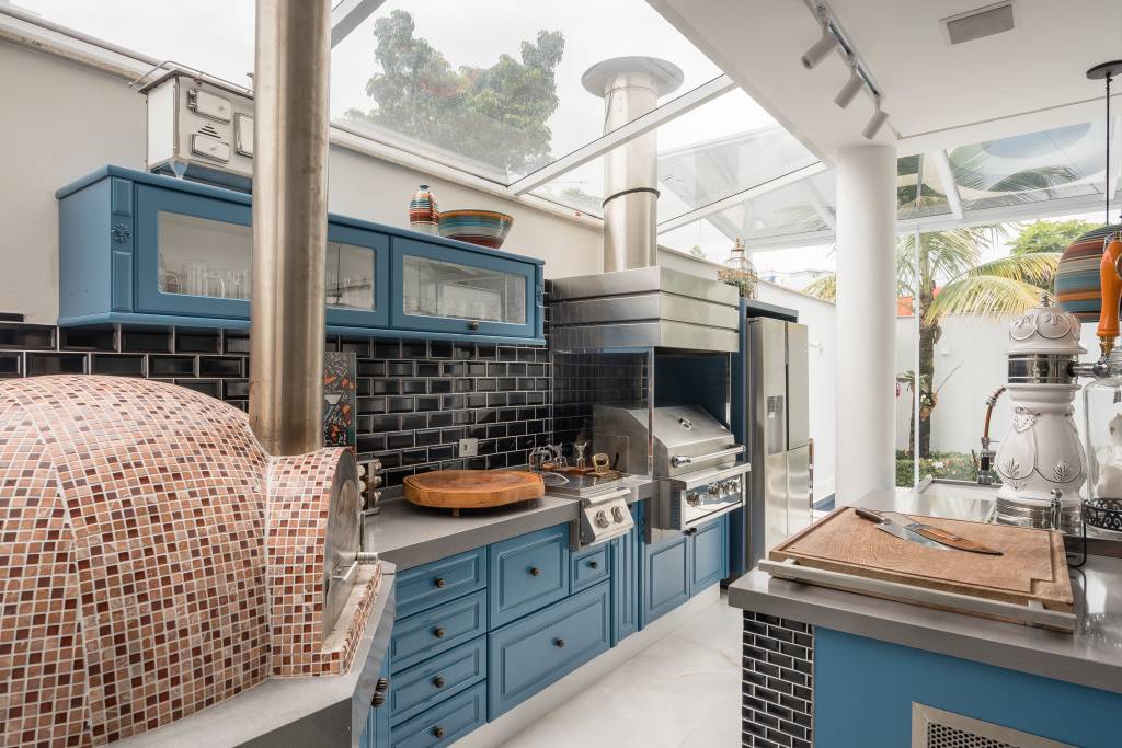 Cozinha com móveis azuis e forno com ladrilhos aparecem na imagem.
