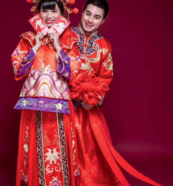 Sisi e Lucas abraçados posando para a câmera com as vestes do casamento chinês (Sisi segura o pacote com moedas)