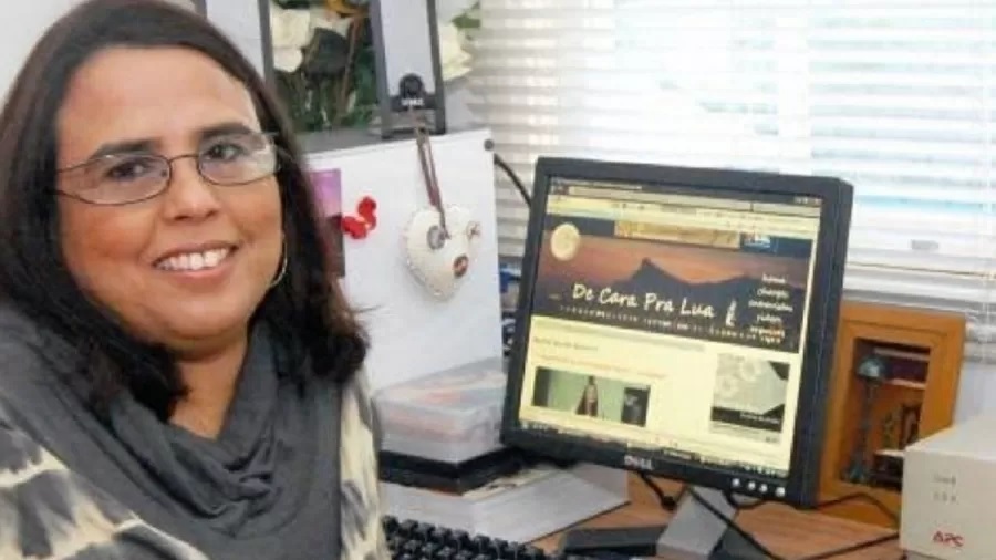 Susan Mello, do blog De Cara pra Lua e pioneira como comentarista de BBB, sorri para foto com tela do computador ao lado.