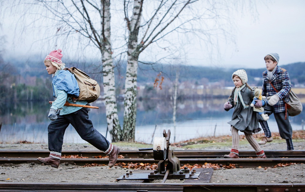 As três crianças do filme, com roupas de frio, corrento sobre um trilho de trem