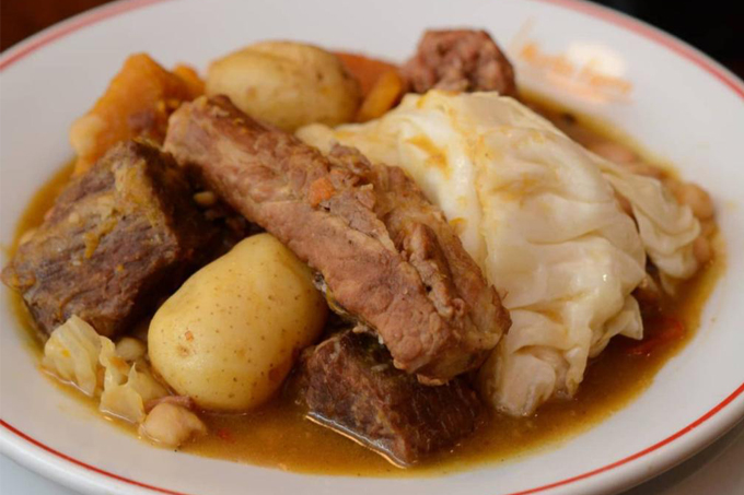 Prato fundo branco com cozido com carne, batata e repolho.