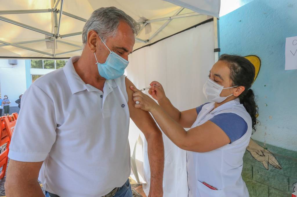 Imagem mostra idoso sendo vacinado por enfermeira em posto de saúde
