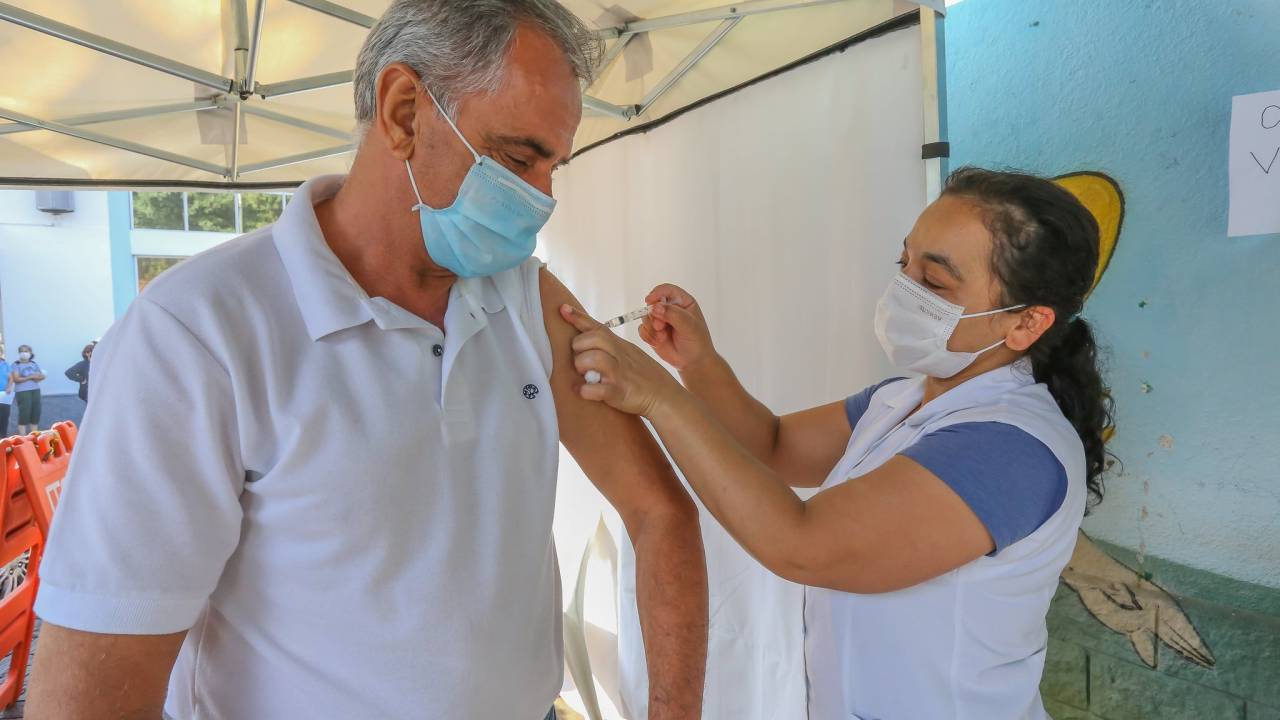 Imagem mostra idoso sendo vacinado por enfermeira em posto de saúde