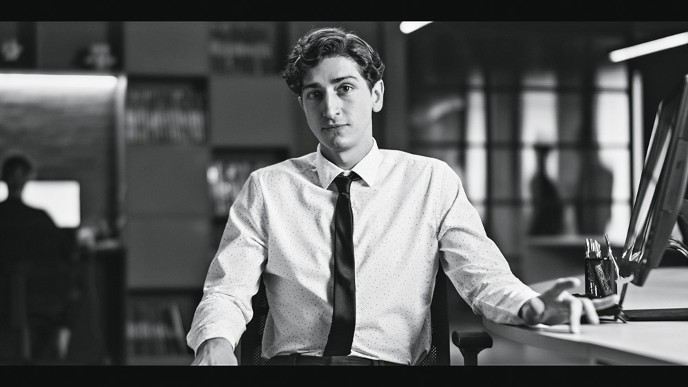 Homem de terno e gravata sentado em um escritório olha para a câmera. Foto em preto e branco