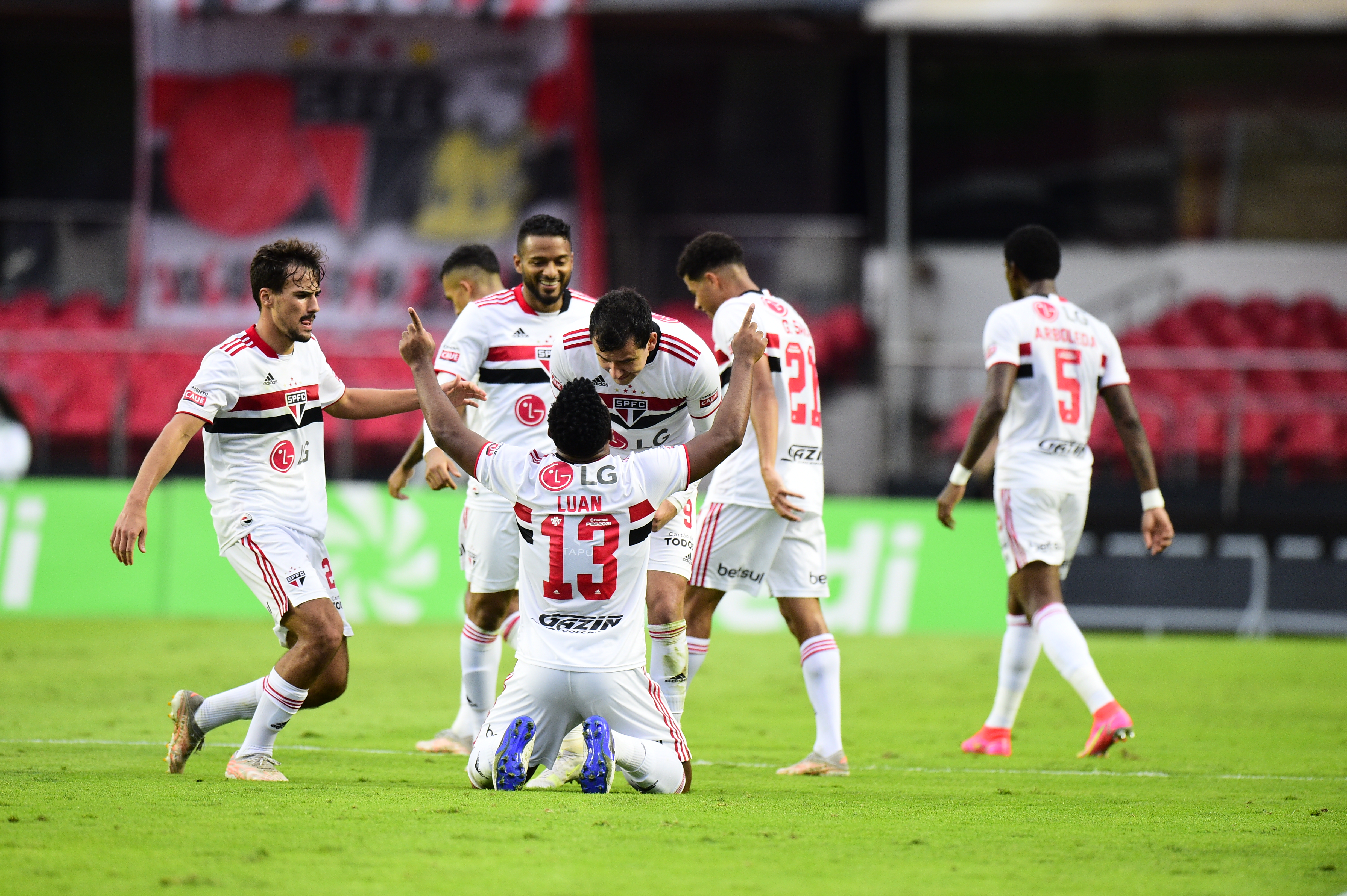 A imagem mostra Luan, ajoelhado, apontando para o céu enquanto comemora o gol do São Paulo cercado pelos companheiros