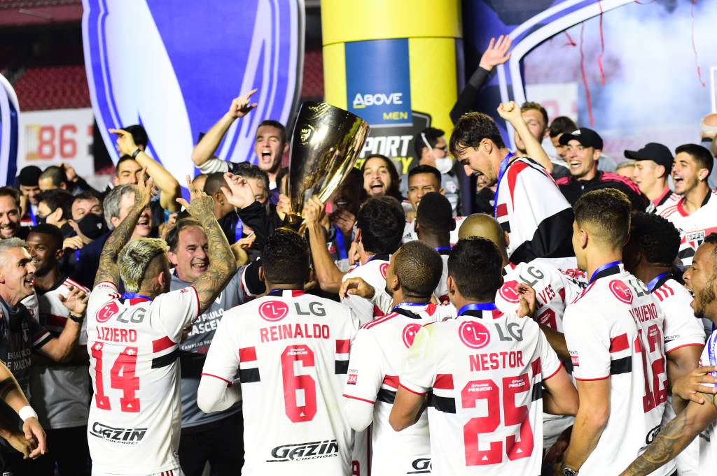 A imagem mostra jogadores do São Paulo em volta do troféu do Campeonato Paulista, todos muito felizes