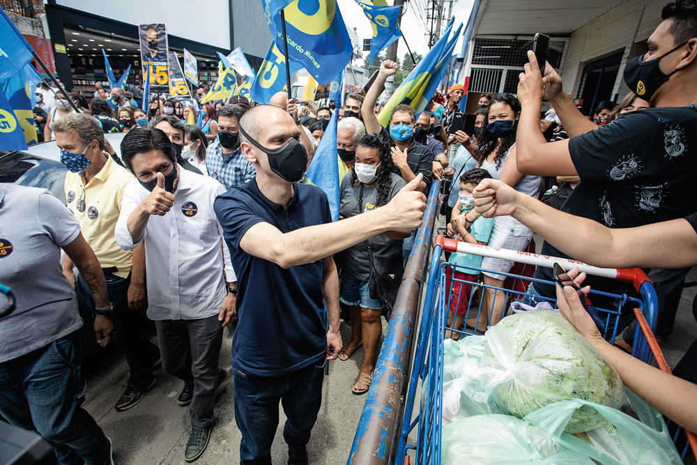 A imagem mostra Covas e Nunes em campanha, nas ruas, cercado de apoiadores e bandeiras com nome e número do ´partido. Eles estão de máscara.