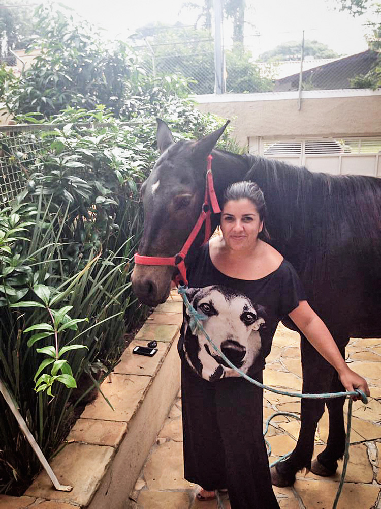 Uma mulher posa com um cavalo ao lado de uma grama vertical