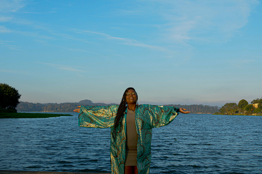 Mulher negra posa com braços abertos em frente a um grande lago