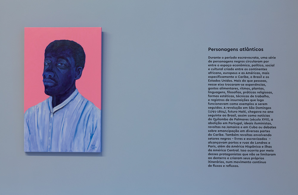Foto mostra parte da exposição Enciclópedia Negra. Mostra foto de um homem negro ao lado da descrição da obra