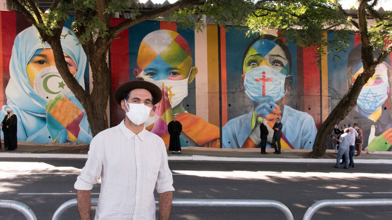 Artista Eduardo Kobra em frente ao mural em homenagem a vítimas de Covid-19, que mostram crianças com máscaras e símbolos de diferentes religiões: união à despeito de diferenças religiosas