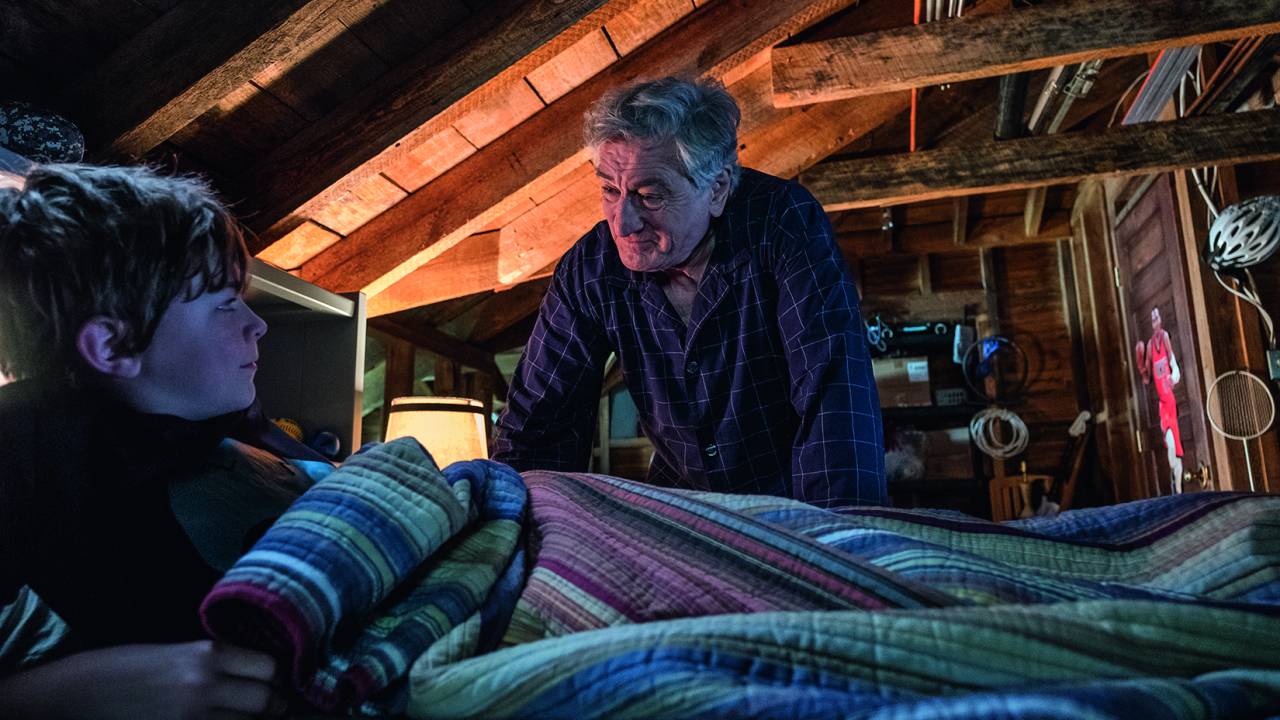 A imagem mostra Fegley deitado em uma cama no sótão e seu De Niro, apoiado na cama, olhando para o jovem
