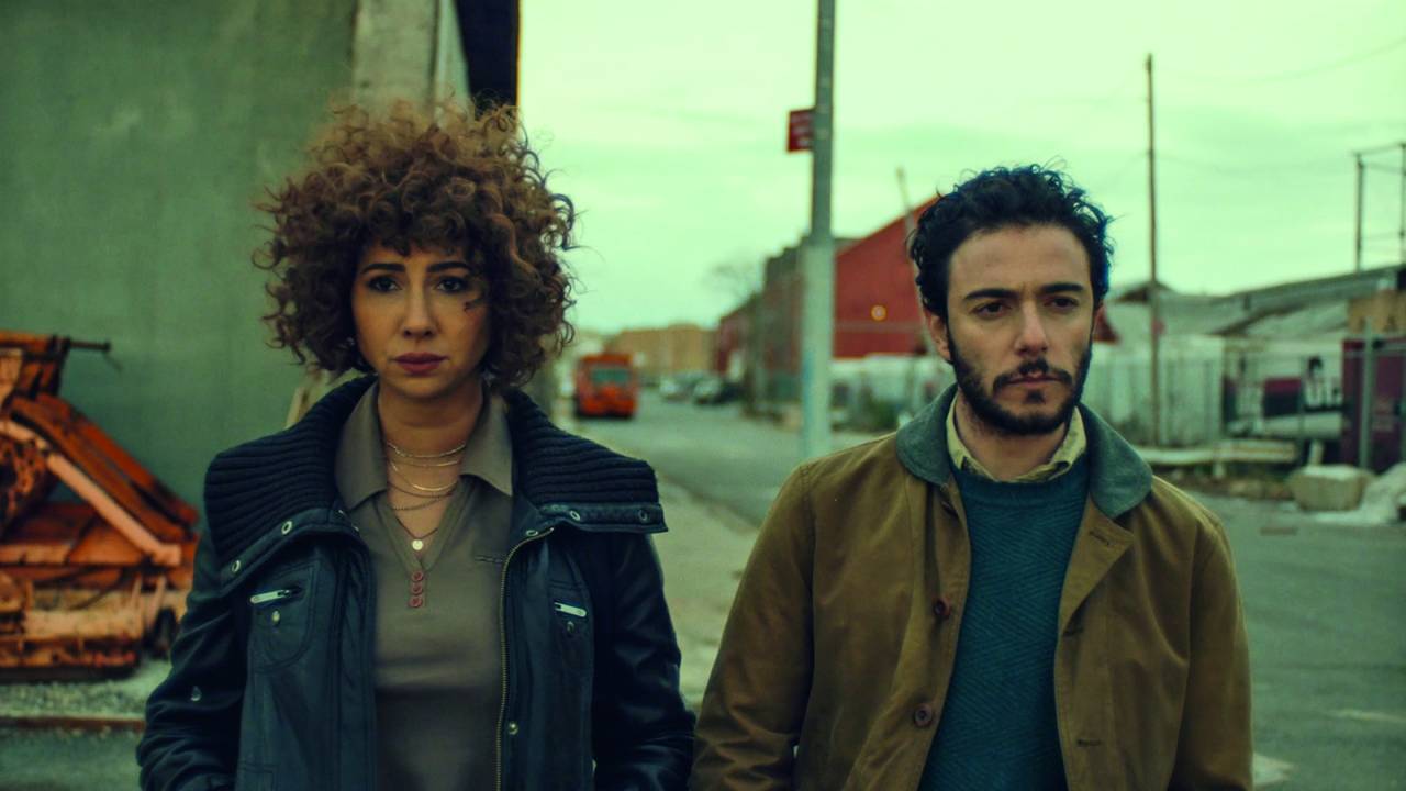 A imagem apresenta dois protagonistas do filme Rosa, andando na rua, olhando com seriedade para frente