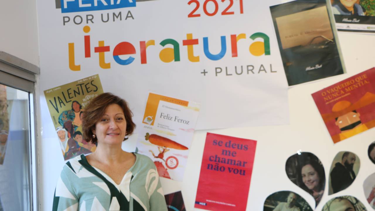 A bibliotecária Rosana Francioli posa de pé em frente a um mural com o título "Literatura Plural".