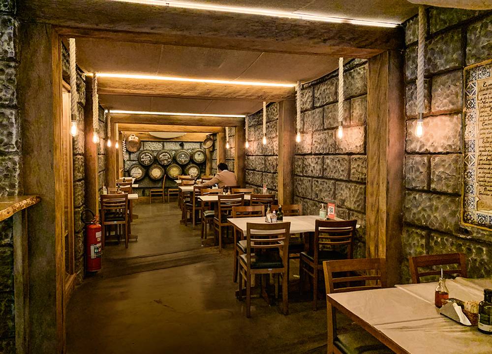 Salão do bar O Mirandês, com um corredor largo e mesas colocadas ao lado da parede à esquerda.