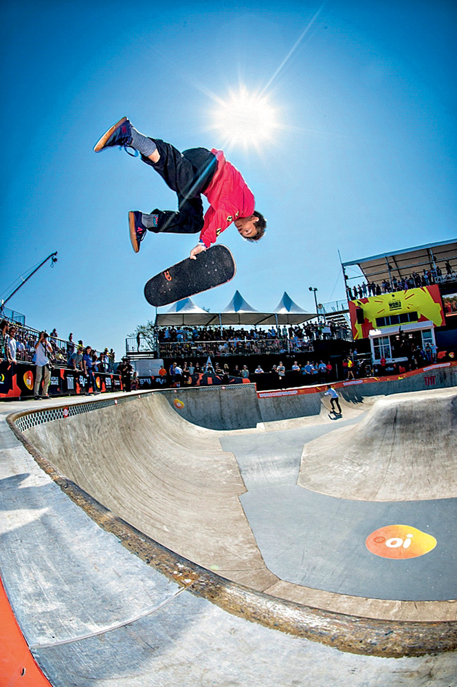 A imagem mostra Luizinho fazendo uma manobra de skate em uma pista rodeada de espectadores durante um dia ensolarado.