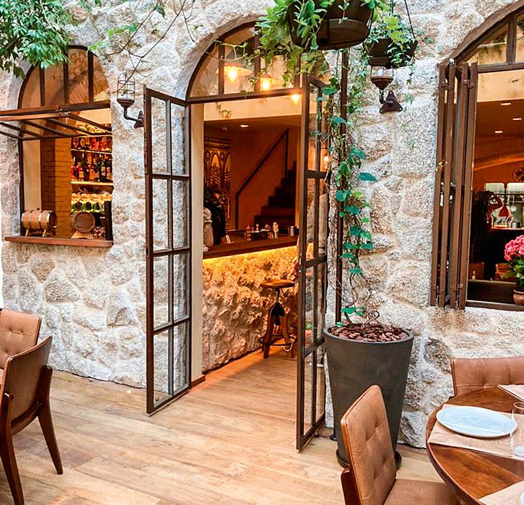 Parte do salão do Piccini Cucina com paredes revestidas de pedra. Parte de mesas com cadeiras nos cantos inferiores.
