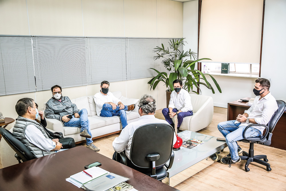 A imagem mostra Ricardo Nunes e seus secreta´rios em uma sala, todos de máscara, durante uma reunião. Eles estão sentados em sofás e cadeiras, relativamente distantes