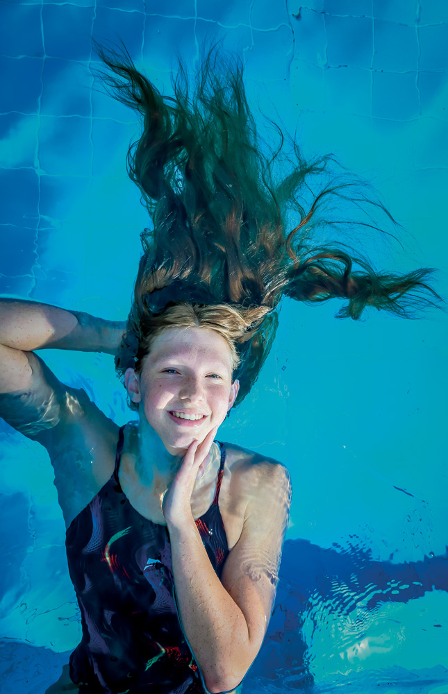 A imagem mostra Stephanie boiando em uma piscina. A câmera a vê de cima, e ela está sorrindo para a foto com todo o corpo submergido com exceção do rosto.