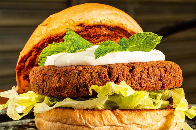 TRADI VEGGIE Foto com bastante zoom no lanche, onde ele é feito com Hambúrguer de falafel no pão integral, contém alface, hortelã e creme azedo