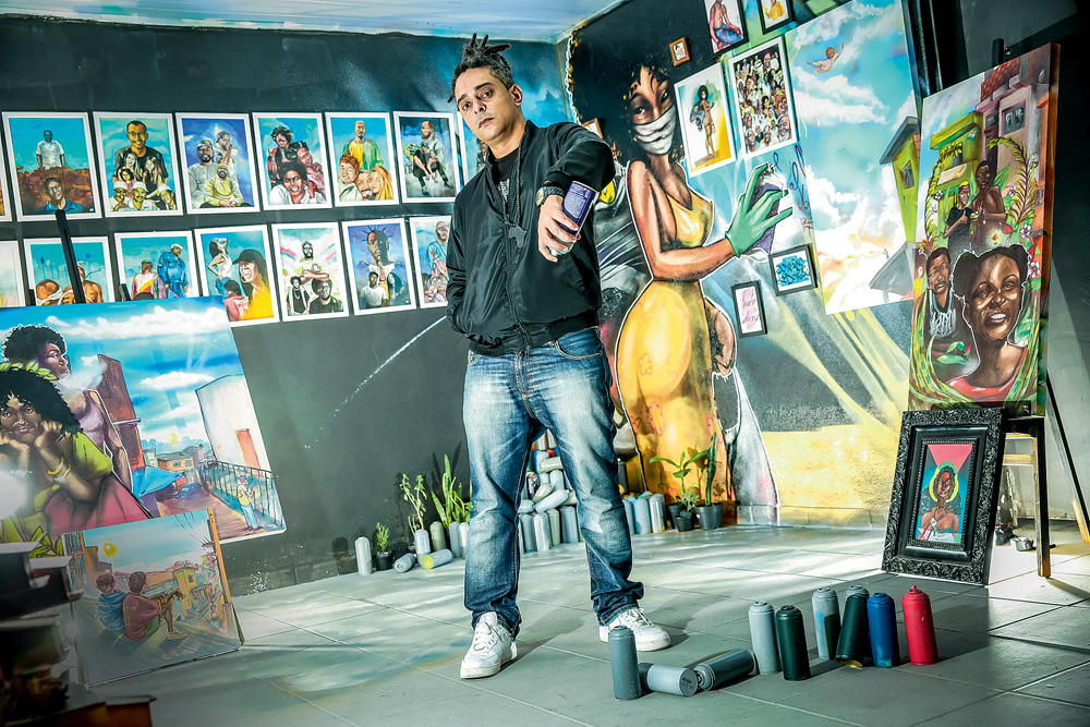 Homem (Val Opni) posa em sua galeria, com vários grafites coloridos pendurados nas paredes a sua volta. Ele segura um spray