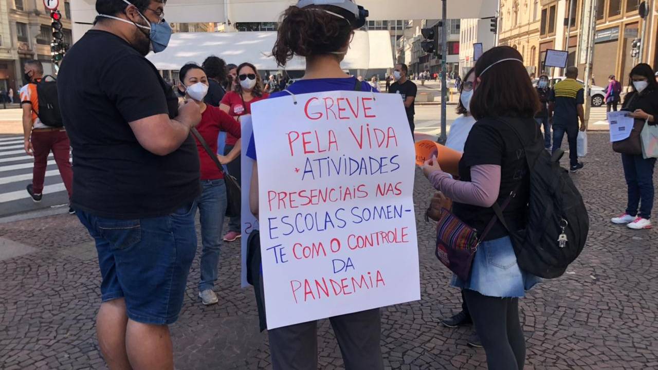 Imagem mostra homem segurando cartaz nas costas que diz: "Greve pela Vida. Atividas presenciais nas escolas somente com o controle da pandemia"