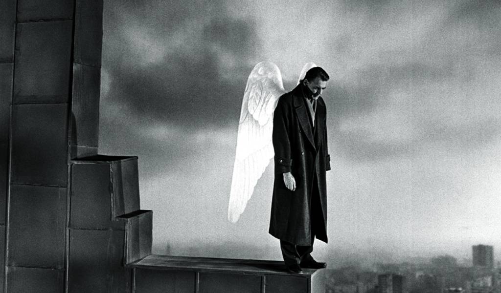 A imagem apresenta um homem no topo de um edifício, na ponta do telhado. Ele tem duas asas de anjo nas costas e a cena aparenta ser melancólica.