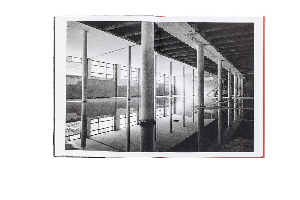Imagem em preto e branco mostra um armazém vazio, com água e reflexos no chão