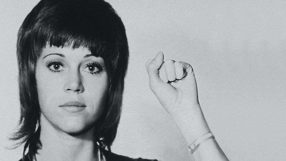 A imagem é um retrato de Jane Fonda em que ela está com o punho esquerdo erguido