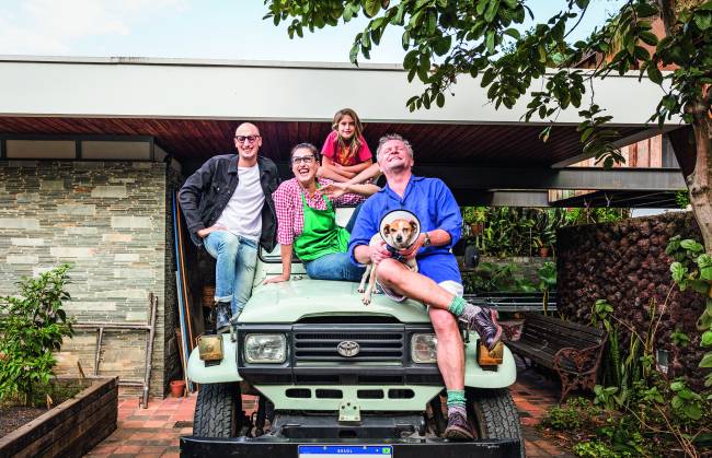 Paola Carosella família Família sobre jipe em frente à casa. Homem à esquerda, Paola Carosella ao centro, criança no topo e homem grisalho com cachorro no colo (à direita).