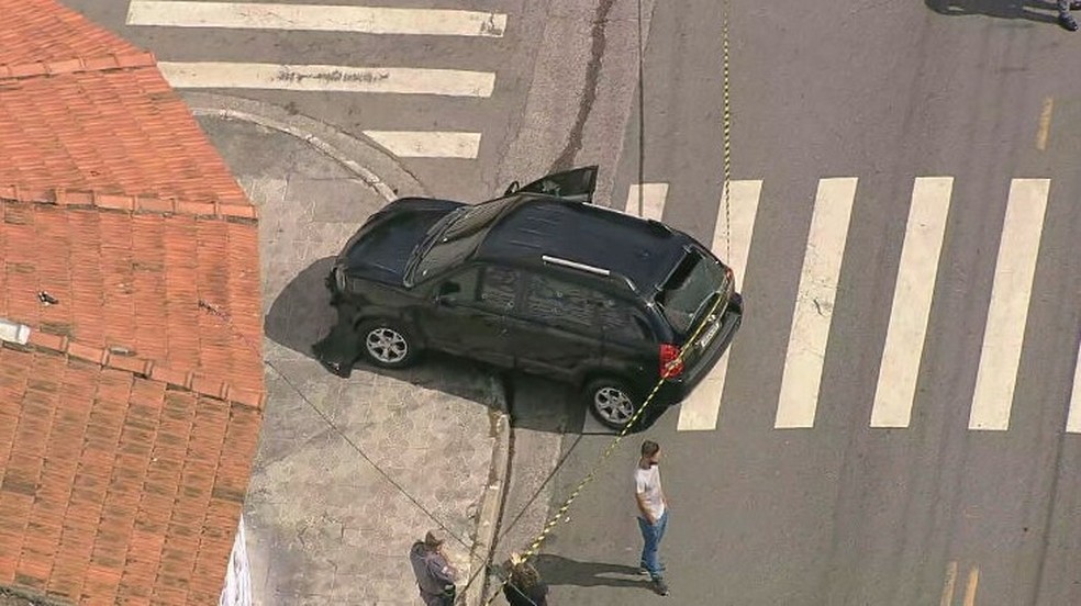 Imagem aérea mostra carro parado próximo de calçada em Avenida, com vidros estilhaçados e buracos de bala