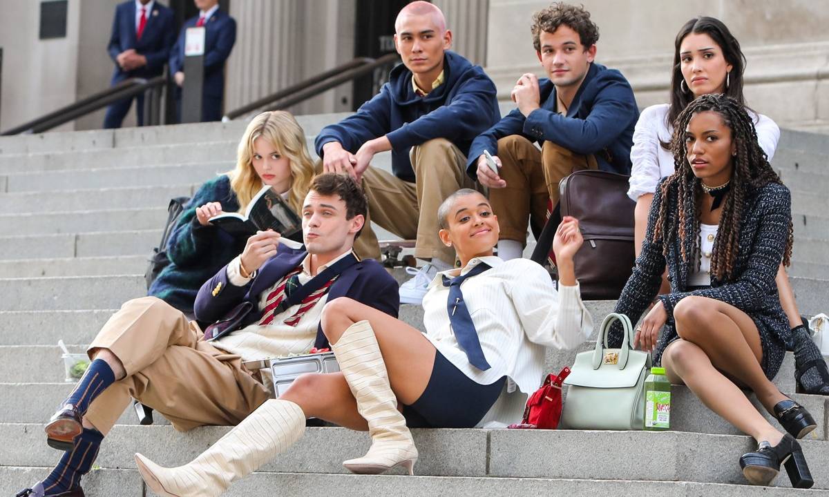 Elenco da série inédita do universo de Gossip Girl sentado em uma escada do colégio em NYC
